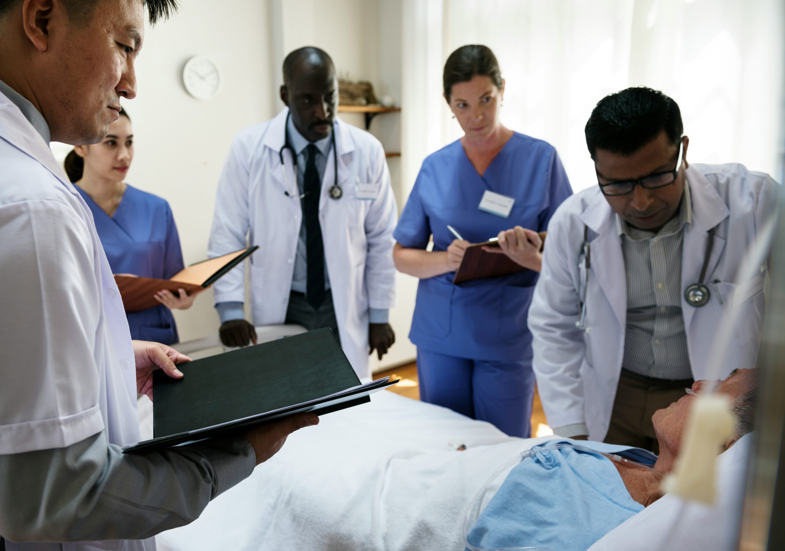 Ärztinnen, Ärzte und Pflegende stehen am Bett eines Patienten und tauschen sich mit Unterlagen in der Hand aus