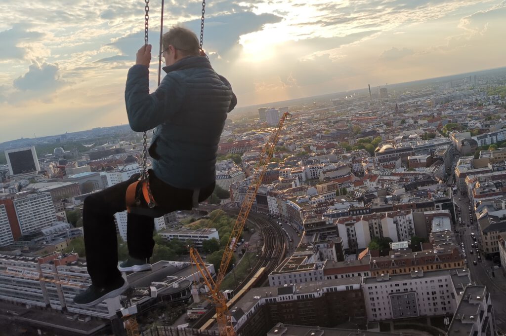 Person an einer Schaukel hoch über einer Stadt – Vertrauen im Veränderungsprozess